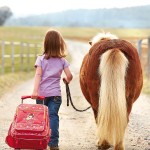 Ein Mädchen führt sein kleines Pony und zieht den Trolley aus der Sigikid-Serie Pony Sue hinterher. EIn schönes Foto.